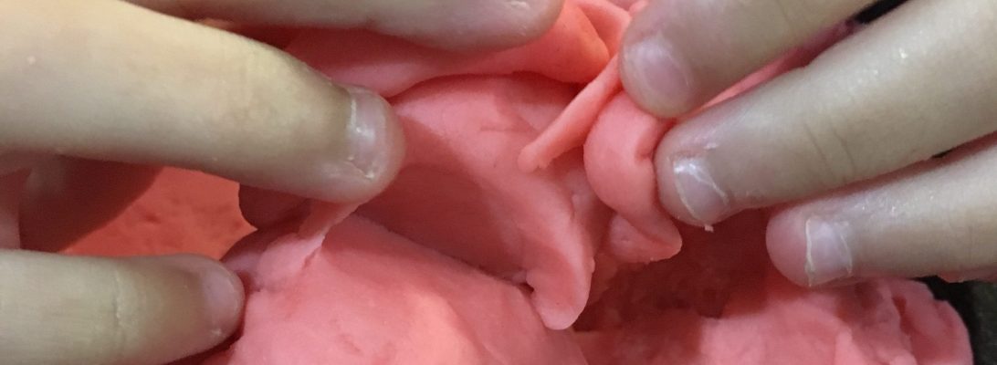 Child playing with homemade playdough at a table, shaping and molding dough with hands