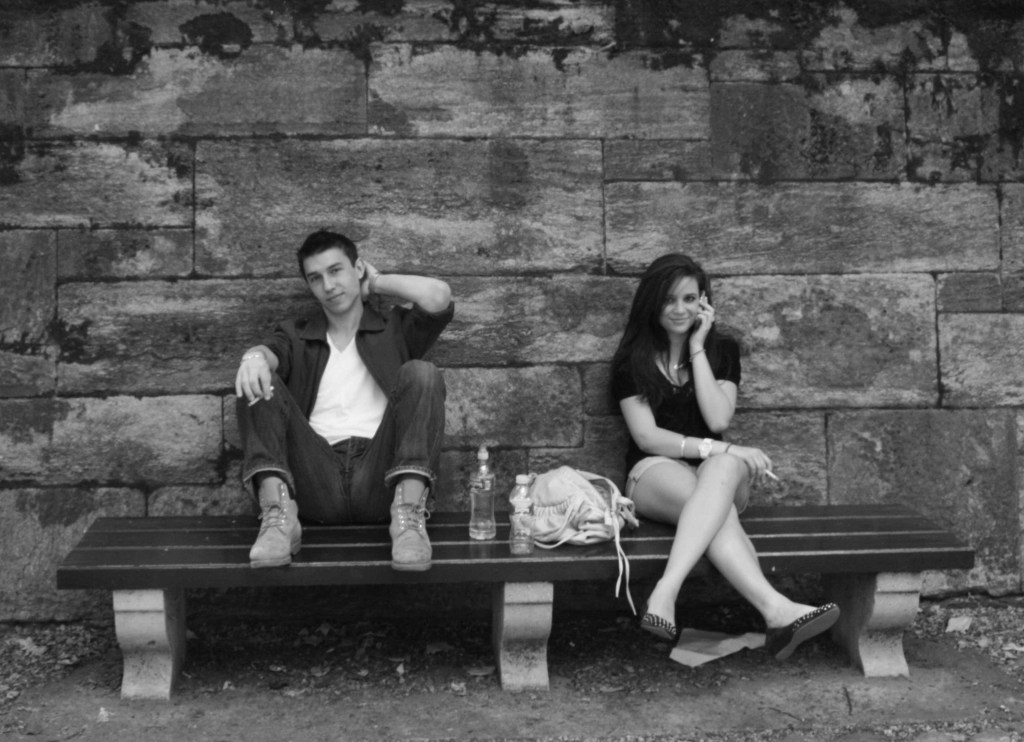 Couple at Central Park in NYC sitting on a bench smoking cigarettes and drinking water